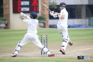 two persons with a bat and ball playing cricket in the ground